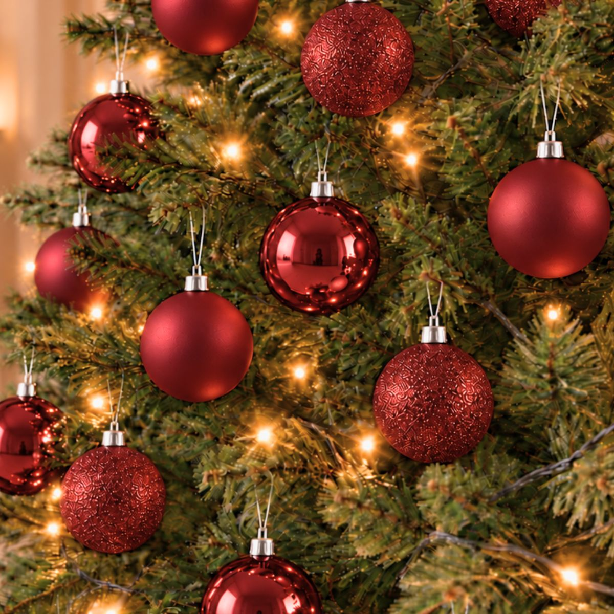 Un sapin de Noël décoré de boules rouges brillantes et mates et de guirlandes lumineuses.