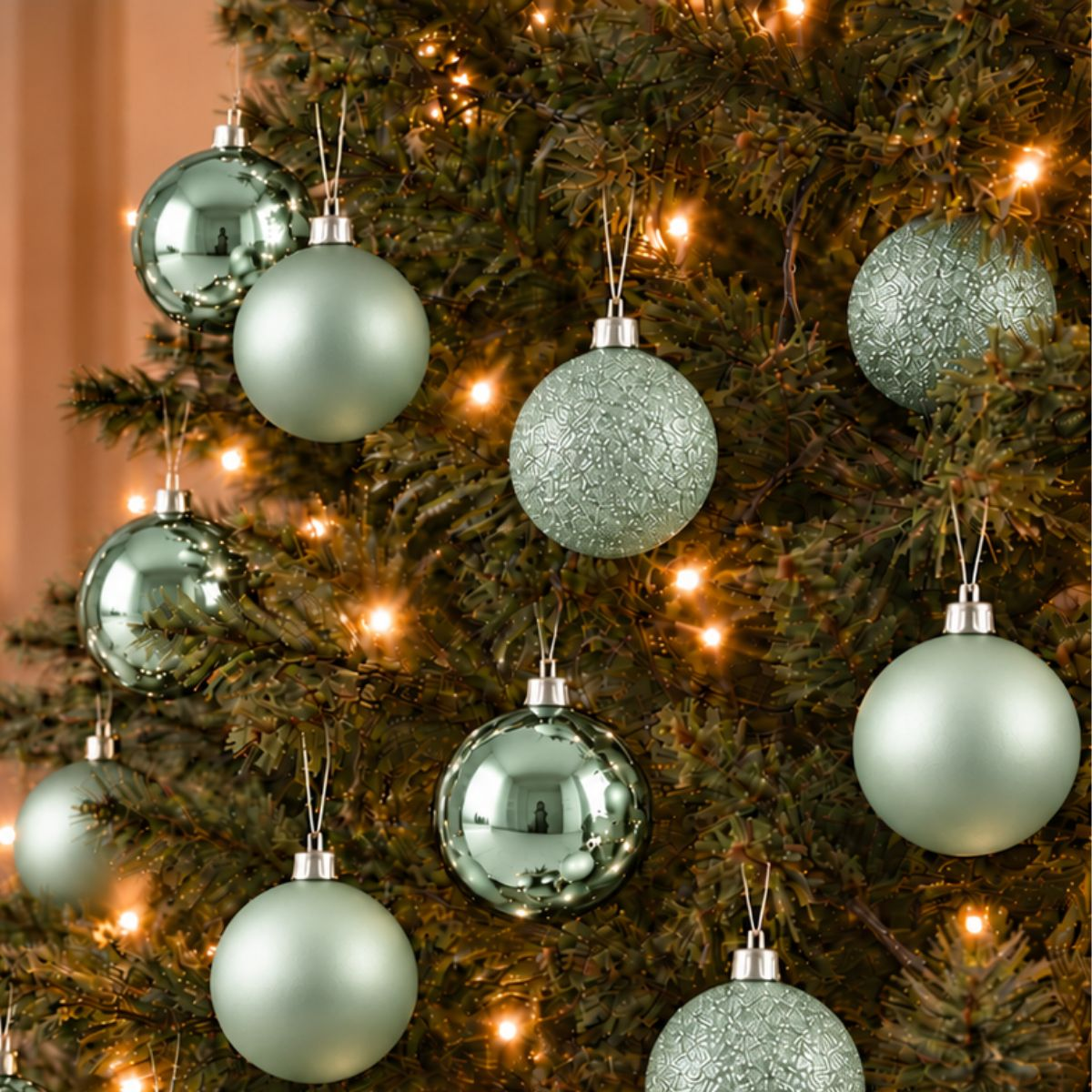 Des boules de Noël vert menthe brillantes et mates sont suspendues à un sapin décoré de lumières.