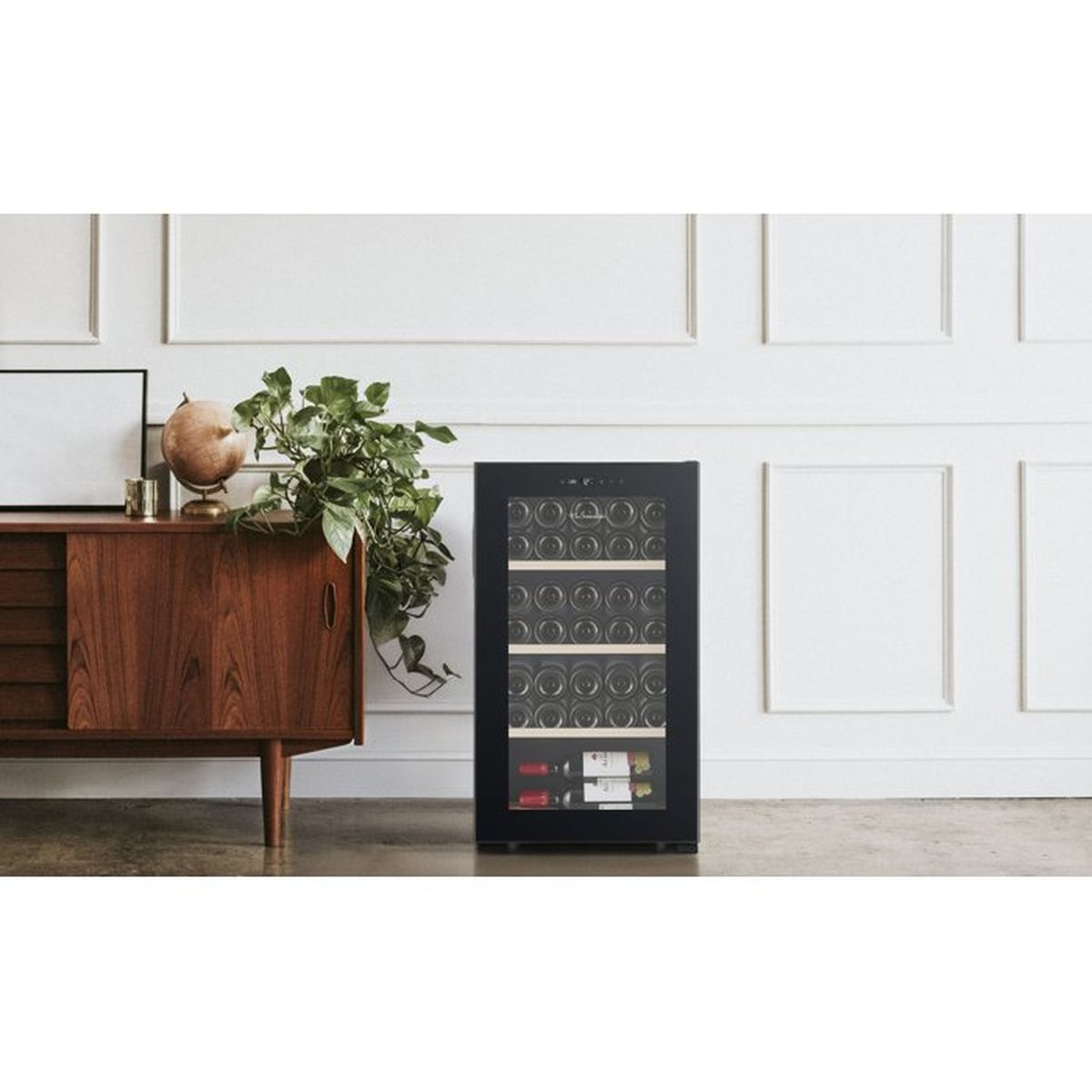 Una vinoteca negra se encuentra junto a un mueble de madera con plantas contra una pared blanca.