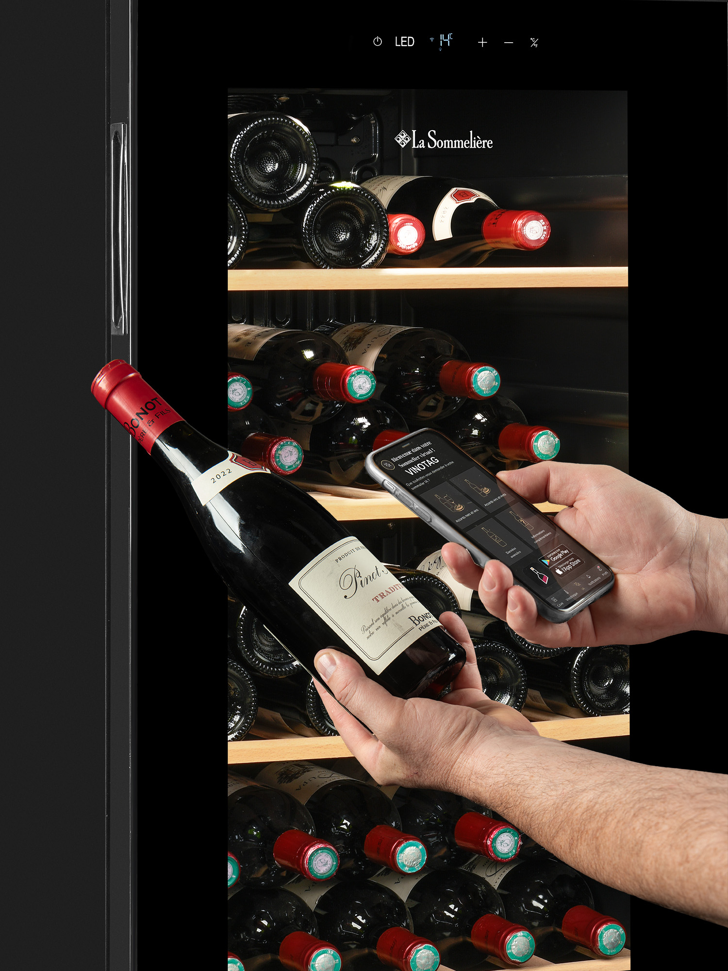 Una persona sostiene una botella de vino y un móvil escaneando su etiqueta frente a una vinoteca llena.