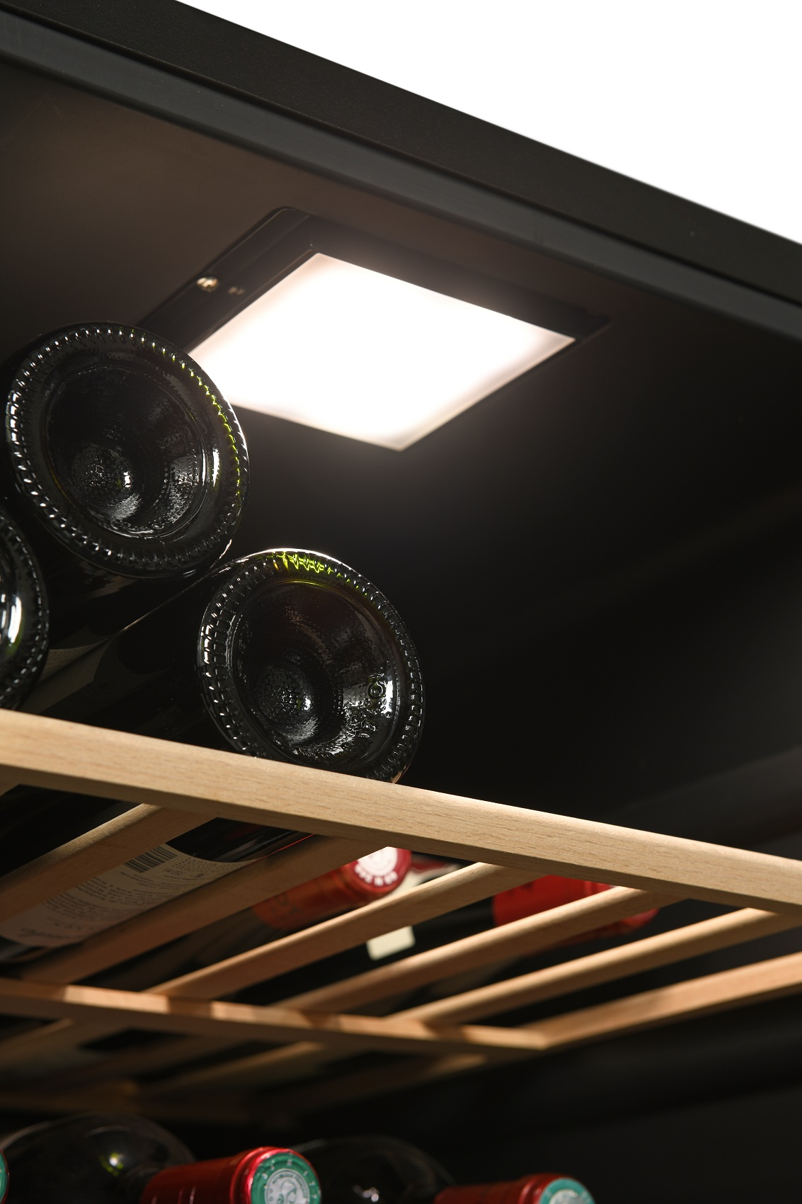 Botellas de vino en un estante de madera bajo una luz LED brillante en una vinoteca.