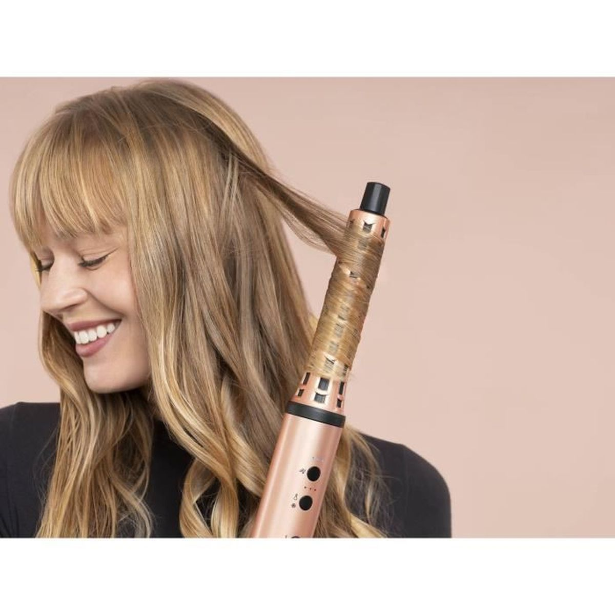 Una donna sorridente avvolge i suoi capelli biondi attorno a un ferro arricciacapelli oro rosa.