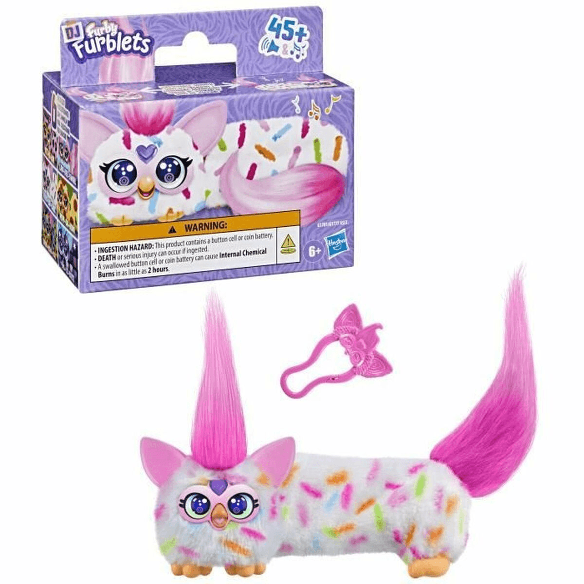 Un juguete Furby Furblets blanco y rosa con chispas, pelo rosa y llavero, junto a su empaque morado.