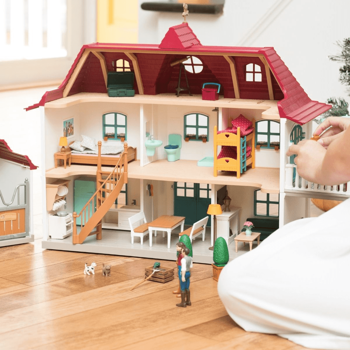 Una gran casa de muñecas de varios pisos con habitaciones amuebladas, figuras en miniatura y muebles en un piso de madera.