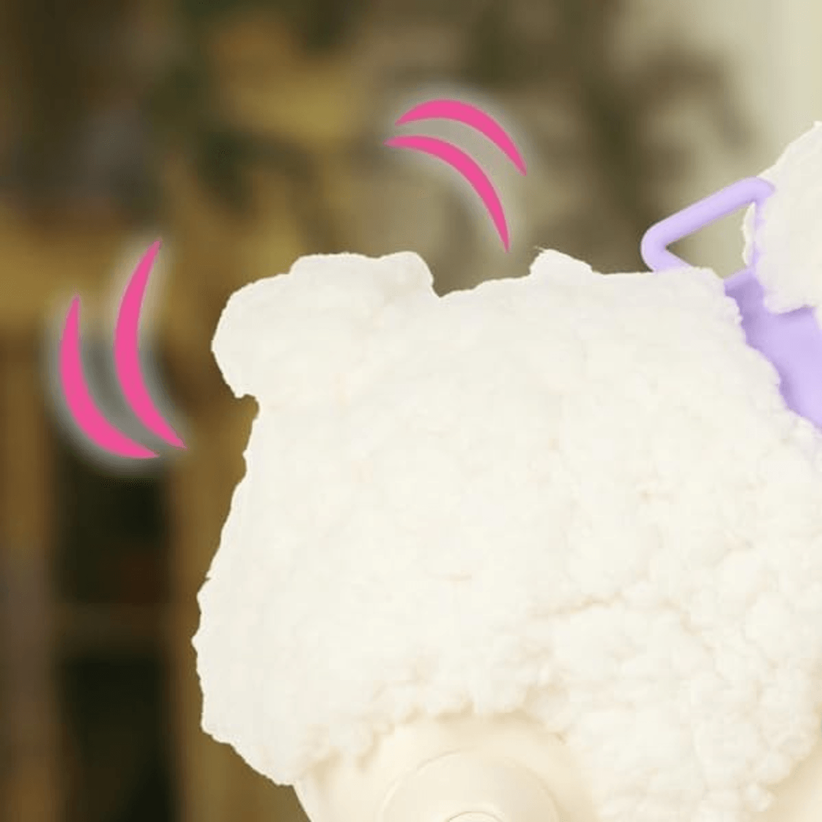 Primer plano de un juguete blanco y esponjoso con mango morado y líneas de movimiento rosas.