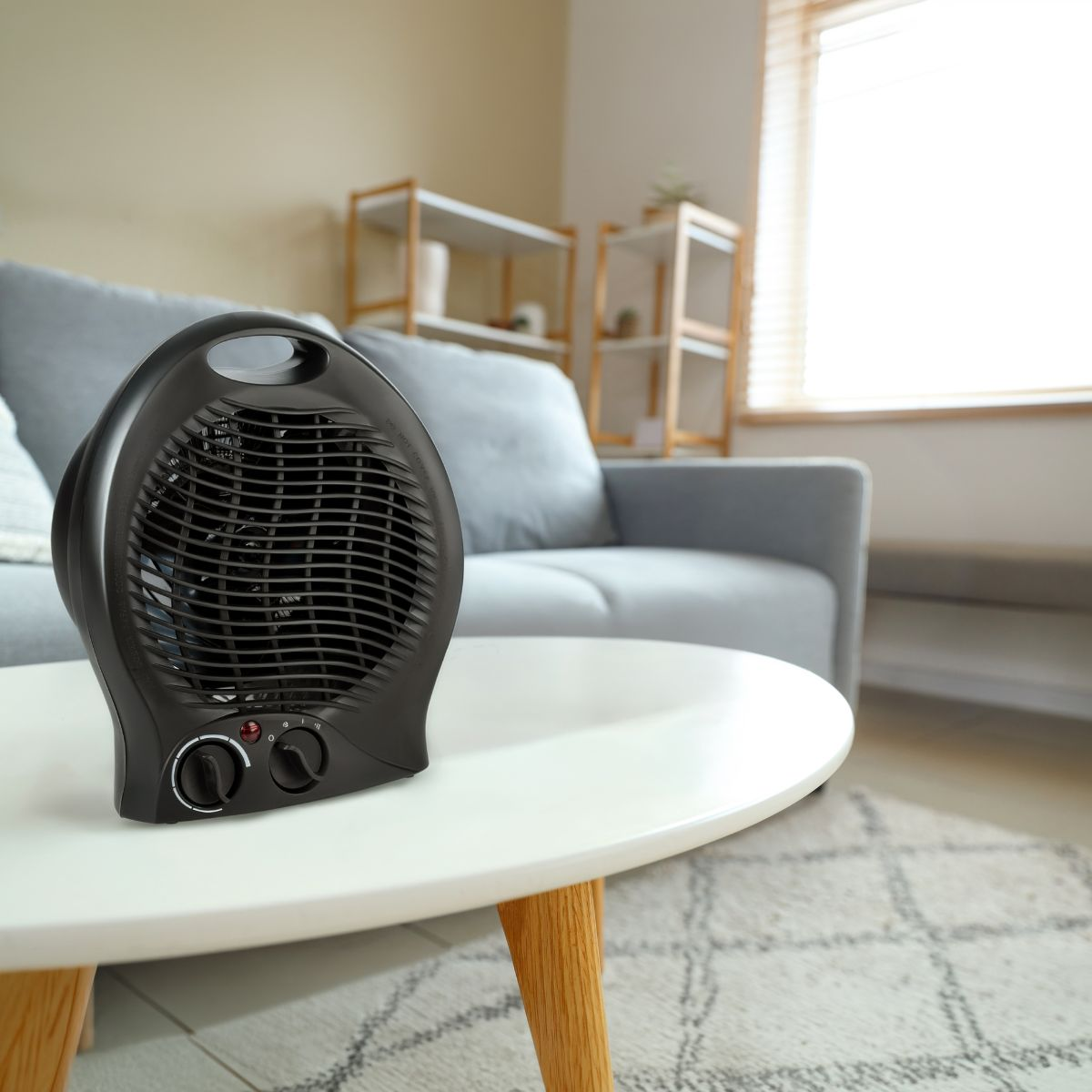Un radiateur soufflant noir repose sur une table basse blanche dans un salon lumineux avec un canapé gris.