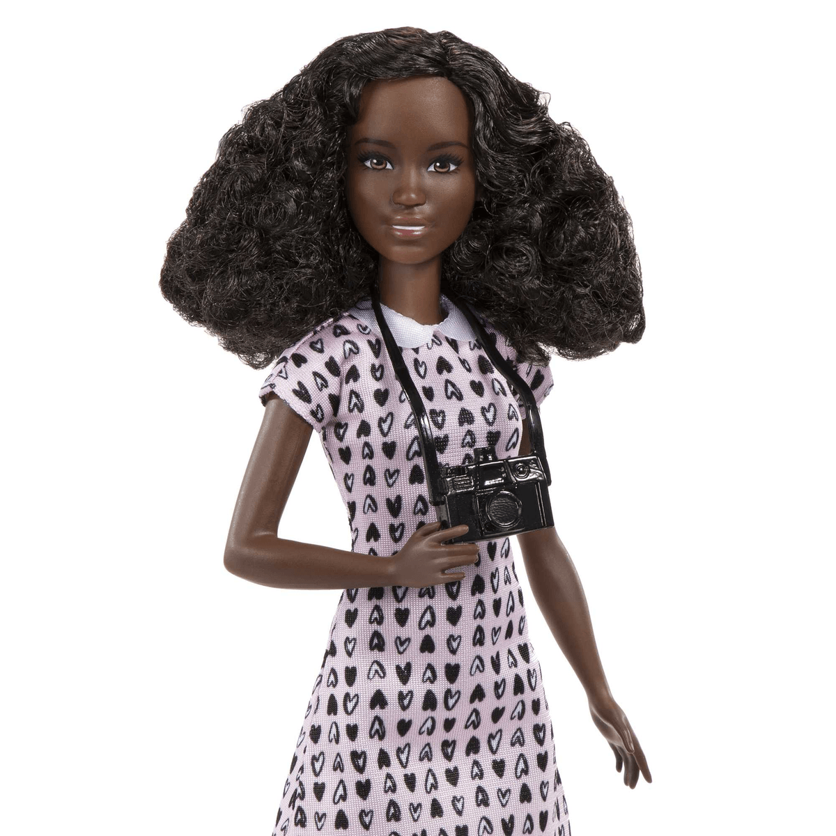 Una muñeca de moda de piel oscura con cabello voluminoso lleva un vestido rosa con corazones negros y una cámara.