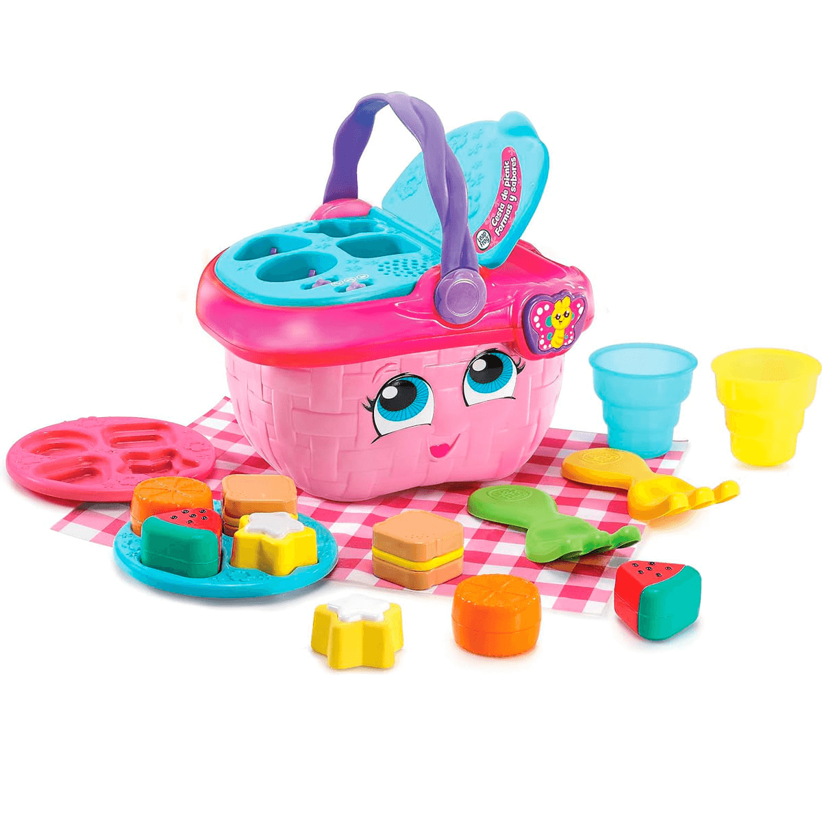 Cesta de picnic de juguete rosa con ojos, rodeada de platos y comida de plástico coloridos sobre un mantel.