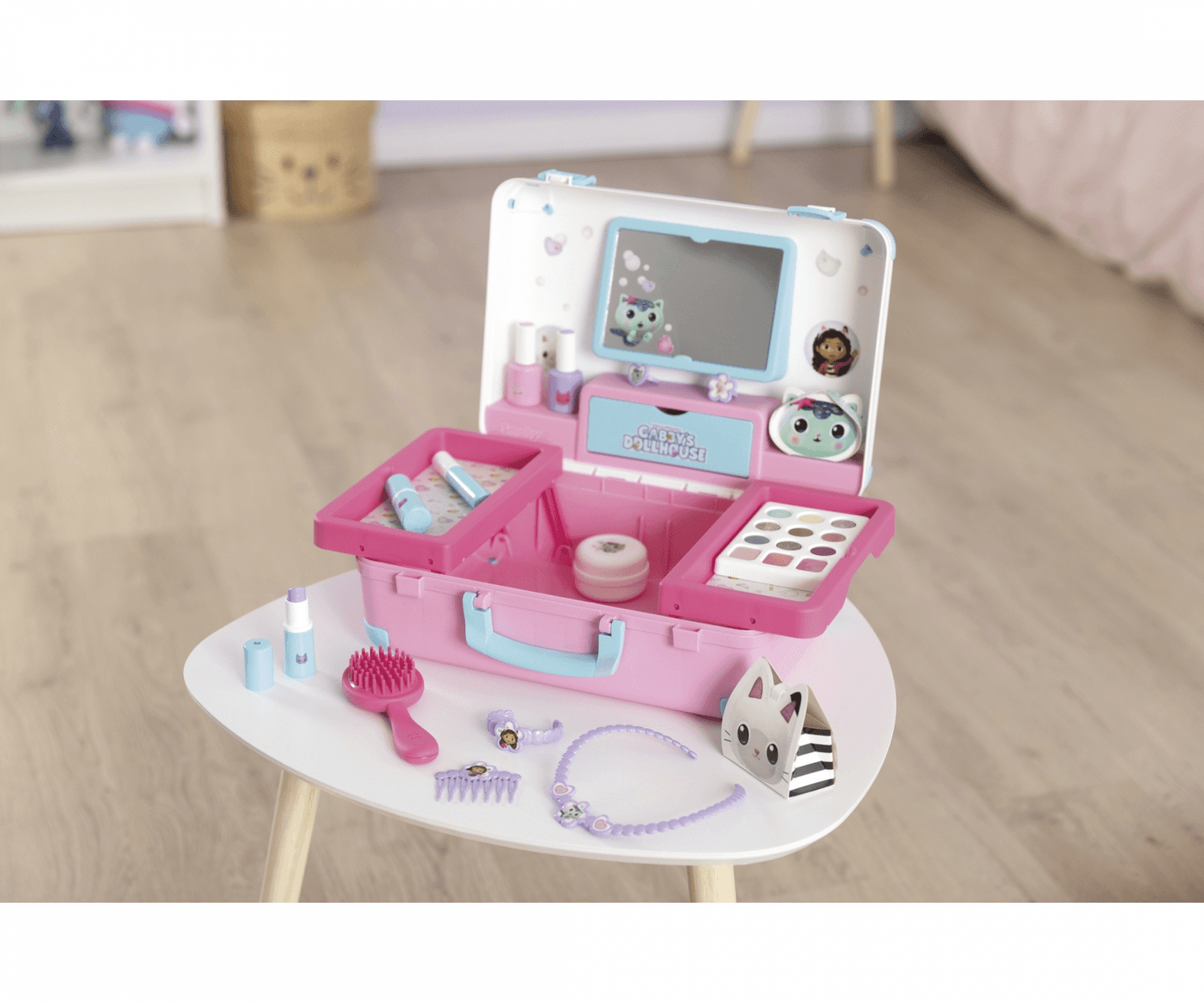Un maletín de juguete rosa con maquillaje, espejo, cepillo y accesorios en una mesa blanca.