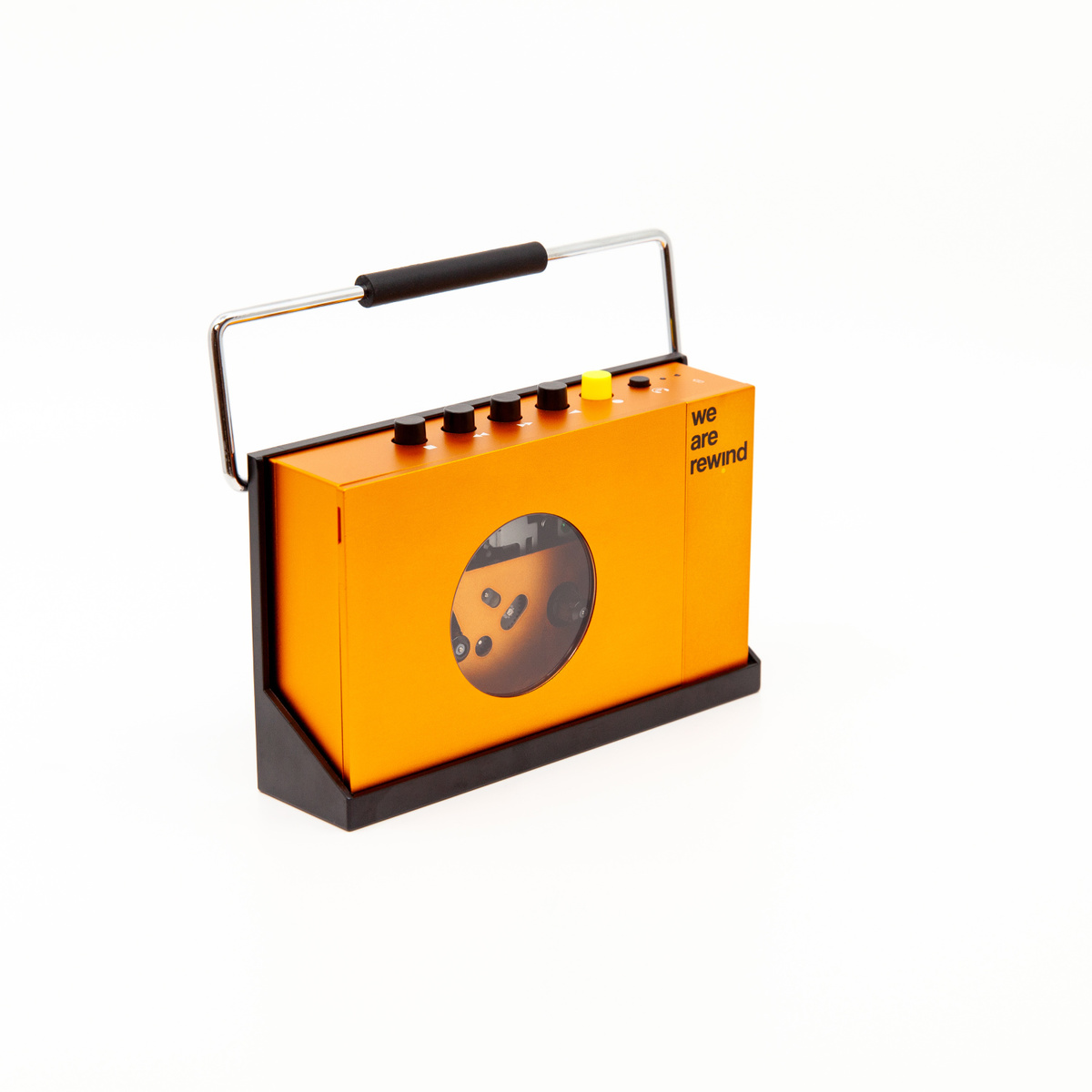 Ein orangefarbener, tragbarer Kassettenrekorder mit Metallgriff, schwarzem Ständer und rundem Fenster vor weißem Hintergrund.