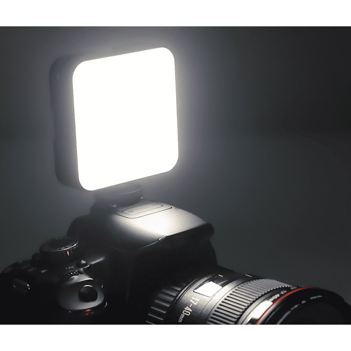 Een helder vierkant LED-paneel is gemonteerd op een zwarte DSLR-camera in een donkere omgeving.