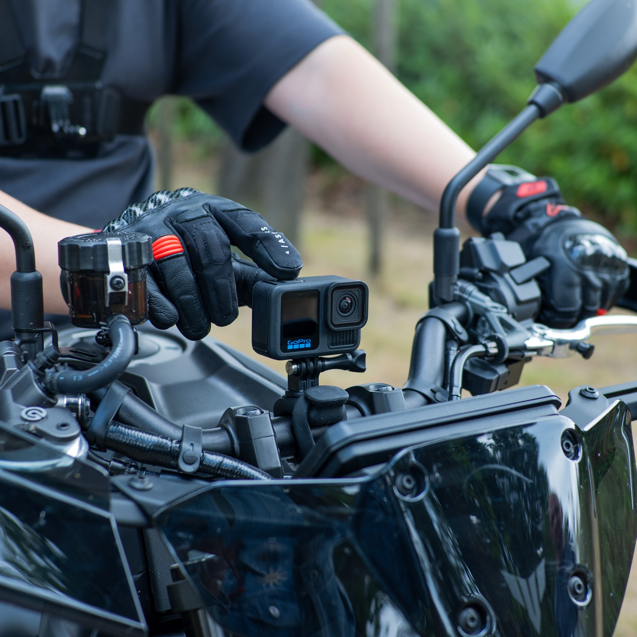 Motorrijder in beschermende kleding bedient een Go Pro-camera op het stuur in de natuur.
