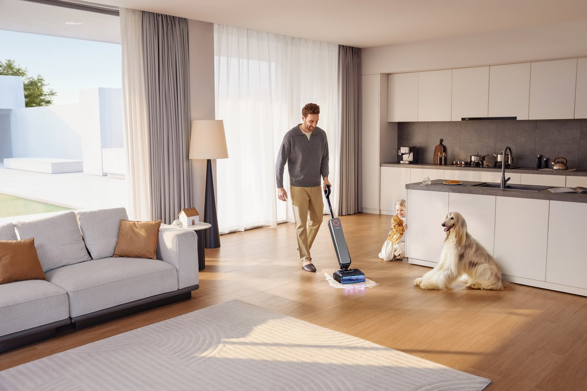 Een man dweilt de vloer in een moderne woonkamer terwijl een hond en kind toekijken.