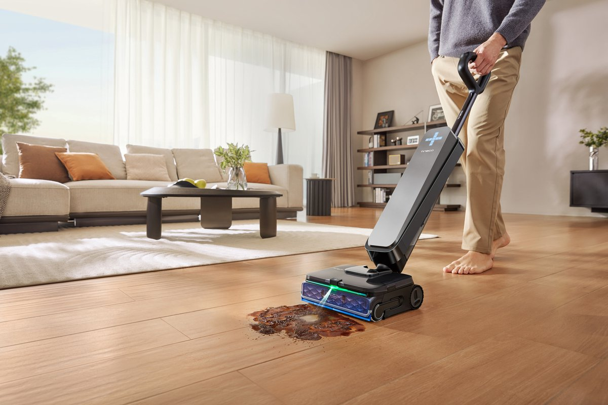 Un homme utilise un balai aspirateur sans fil pour nettoyer une tache collante sur le parquet du salon.