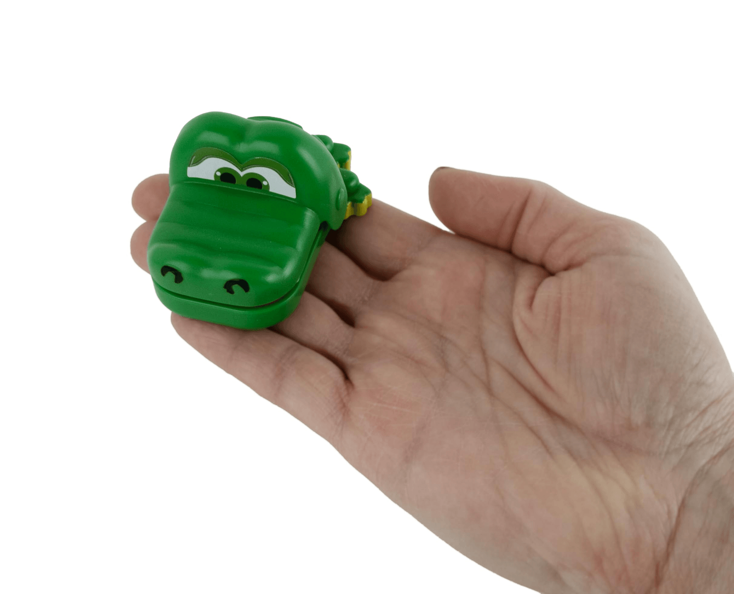 Une main ouverte tient un petit crocodile jouet vert aux grands yeux blancs sur fond blanc.