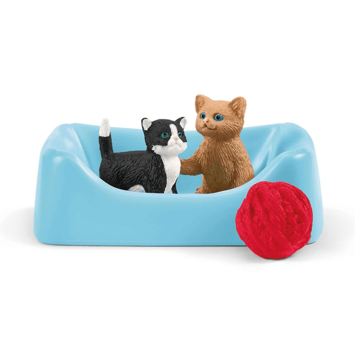 Zwei Katzenfiguren in einem blauen Körbchen, daneben ein roter Wollknäuel auf weißem Hintergrund.