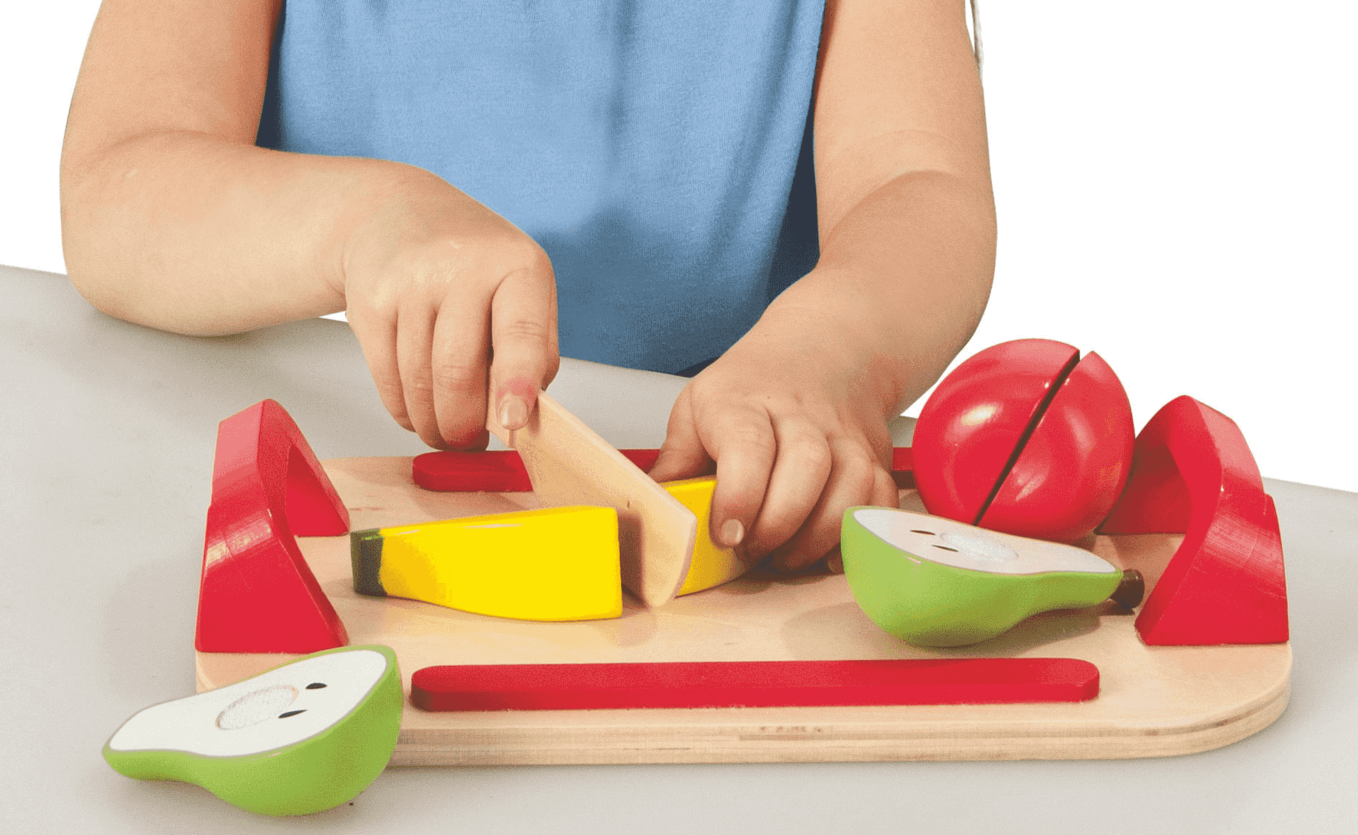 Un niño usa un cuchillo de juguete para cortar fruta de madera en una tabla.
