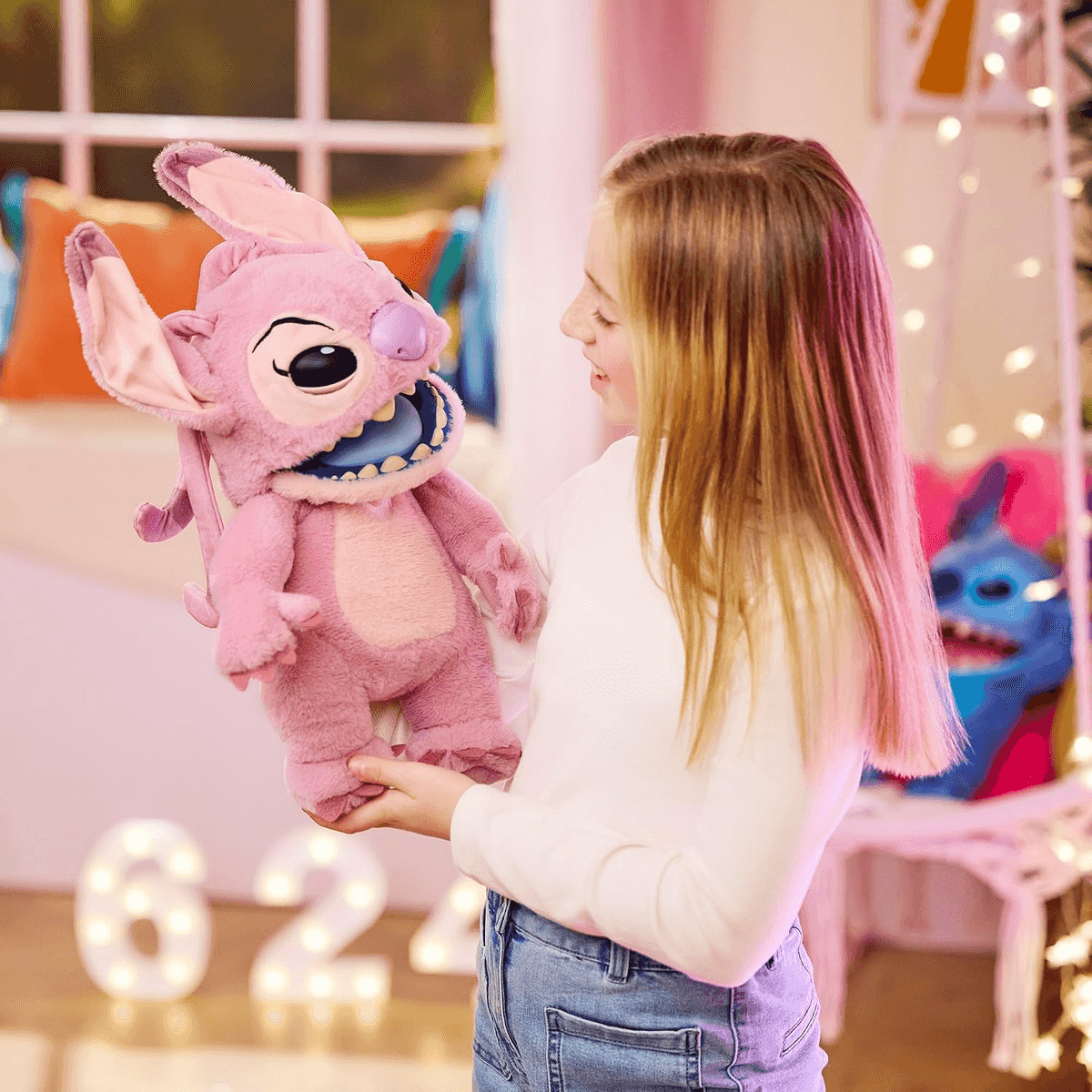 Una niña rubia sostiene un gran peluche rosa de Stitch en una habitación.