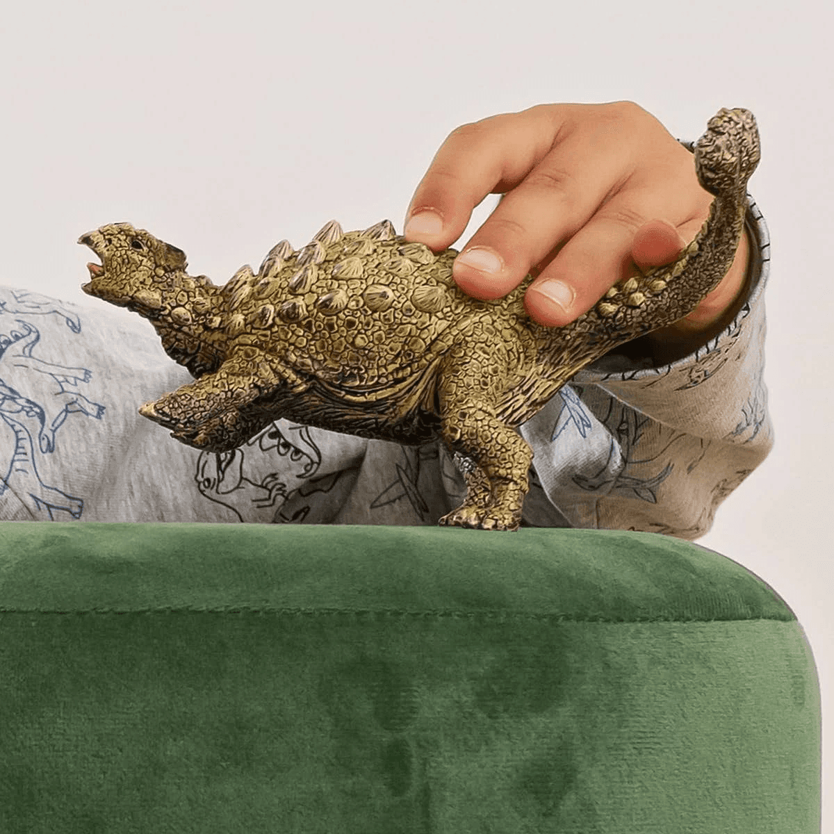 Un niño con suéter estampado toca un juguete de Ankylosaurus en un cojín verde.