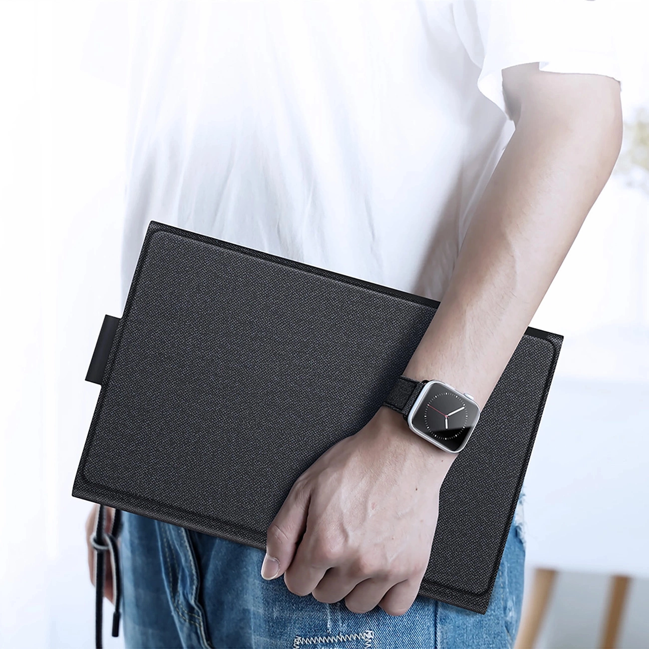 Una persona con camicia bianca e jeans blu tiene una custodia nera per tablet e indossa uno smartwatch.