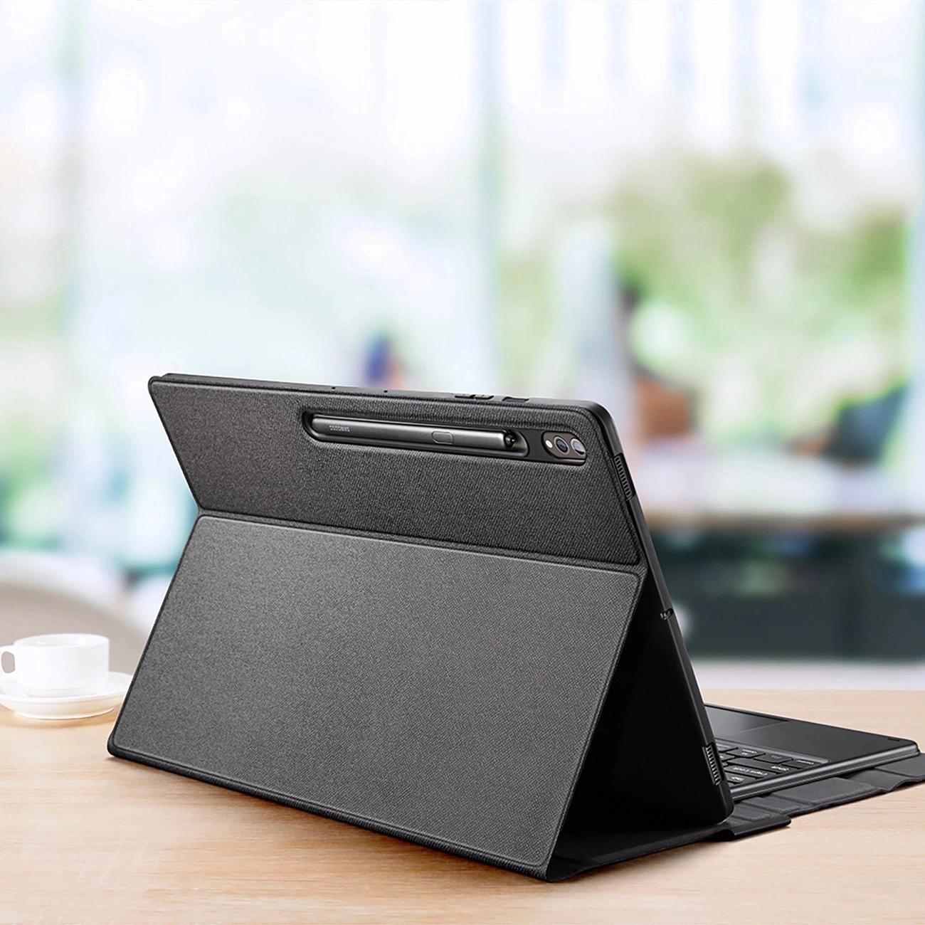 Un tablet nero con custodia con tastiera su una scrivania in legno, con sfondo sfocato.