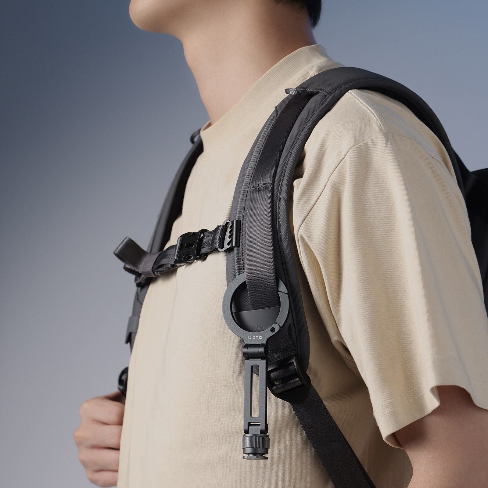 Ein Mensch trägt einen beige farbenen Pullover und einen dunkelgrauen Rucksack mit Brustgurt und Halterungen.