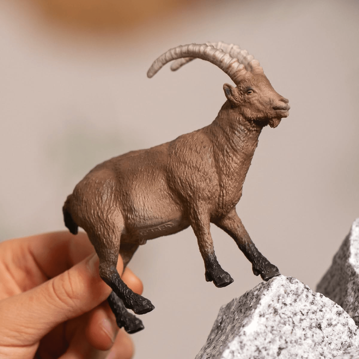 Una mano sostiene una figura de íbice marrón con cuernos largos sobre una roca.