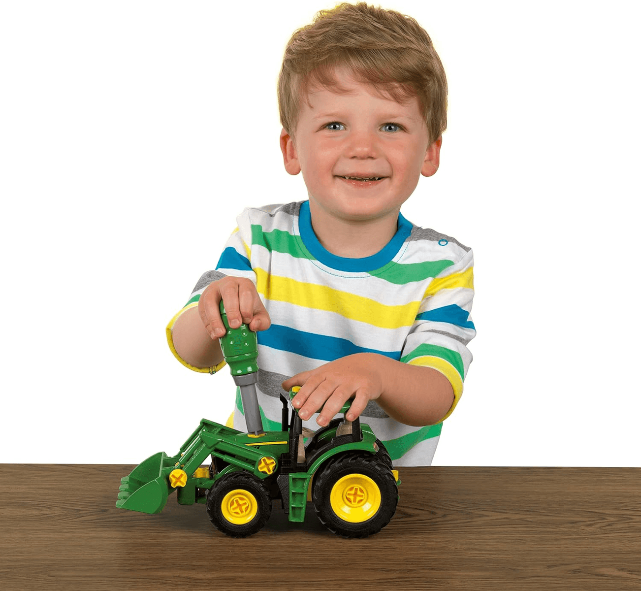 Un niño con camisa a rayas ensambla un tractor de juguete verde en una mesa.