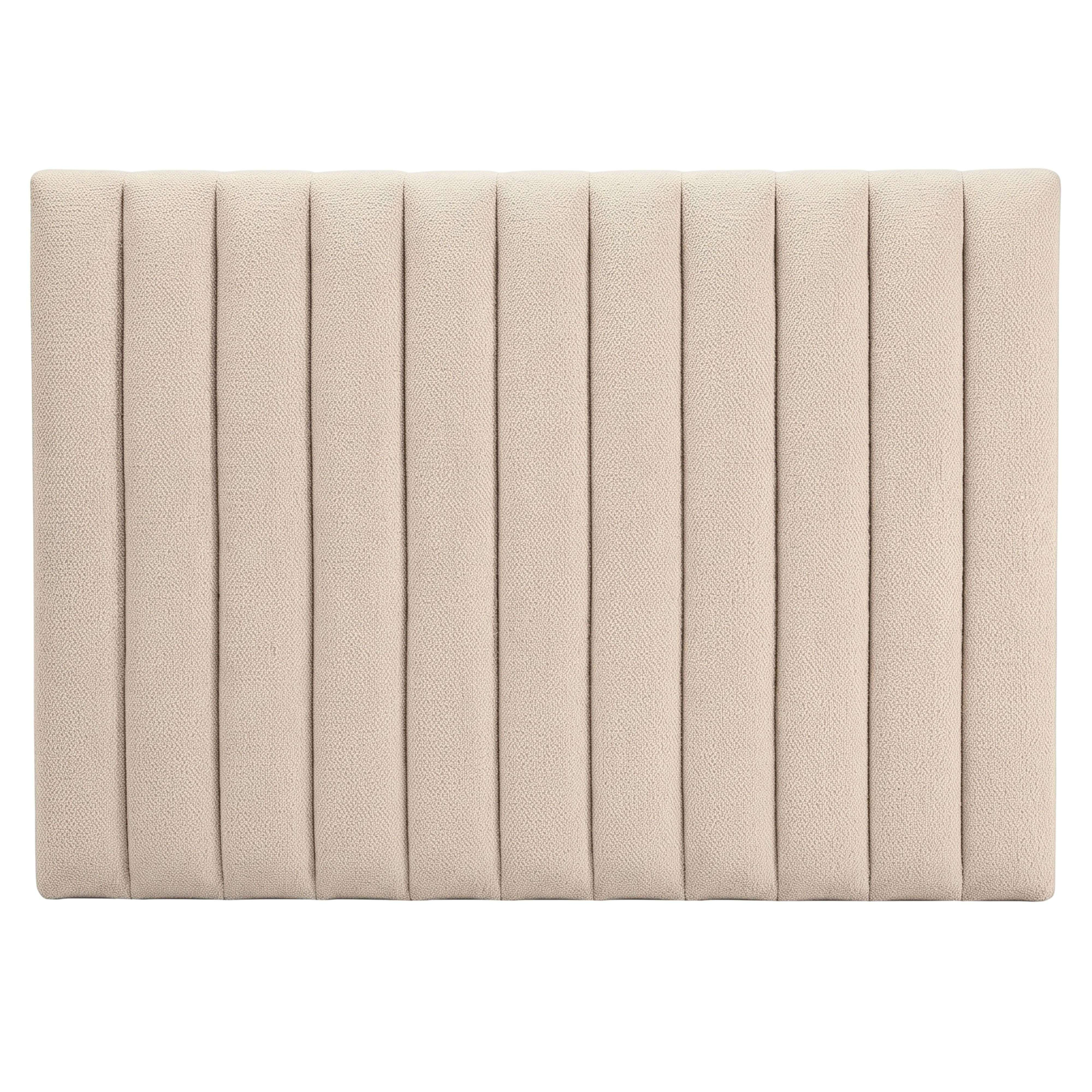 Un cabecero tapizado en beige con canales verticales acolchados sobre fondo liso.