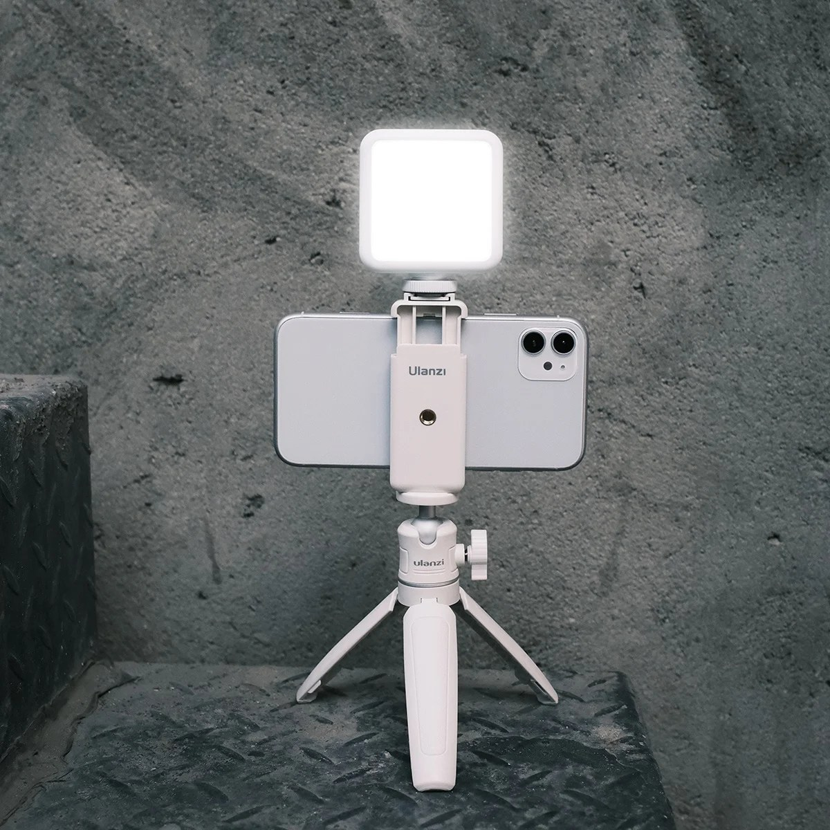 Un smartphone blanc sur trépied avec une petite lampe LED sur un fond gris rugueux.