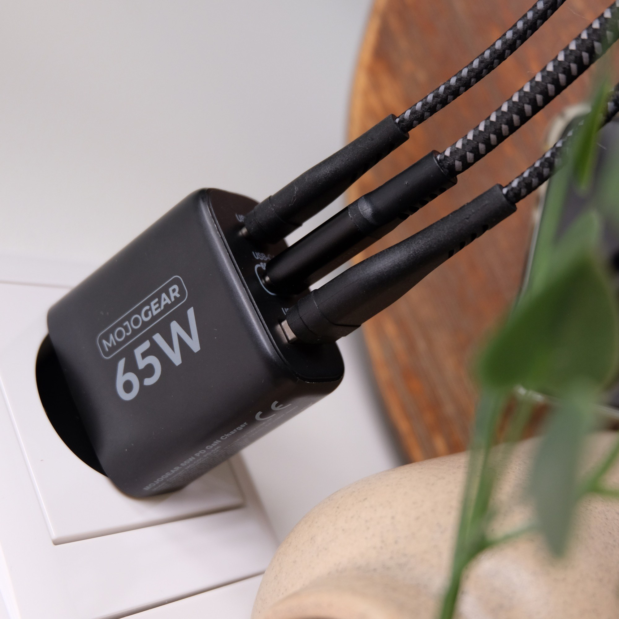 Un chargeur noir MojoGear 65W est branché sur une prise murale avec trois câbles.