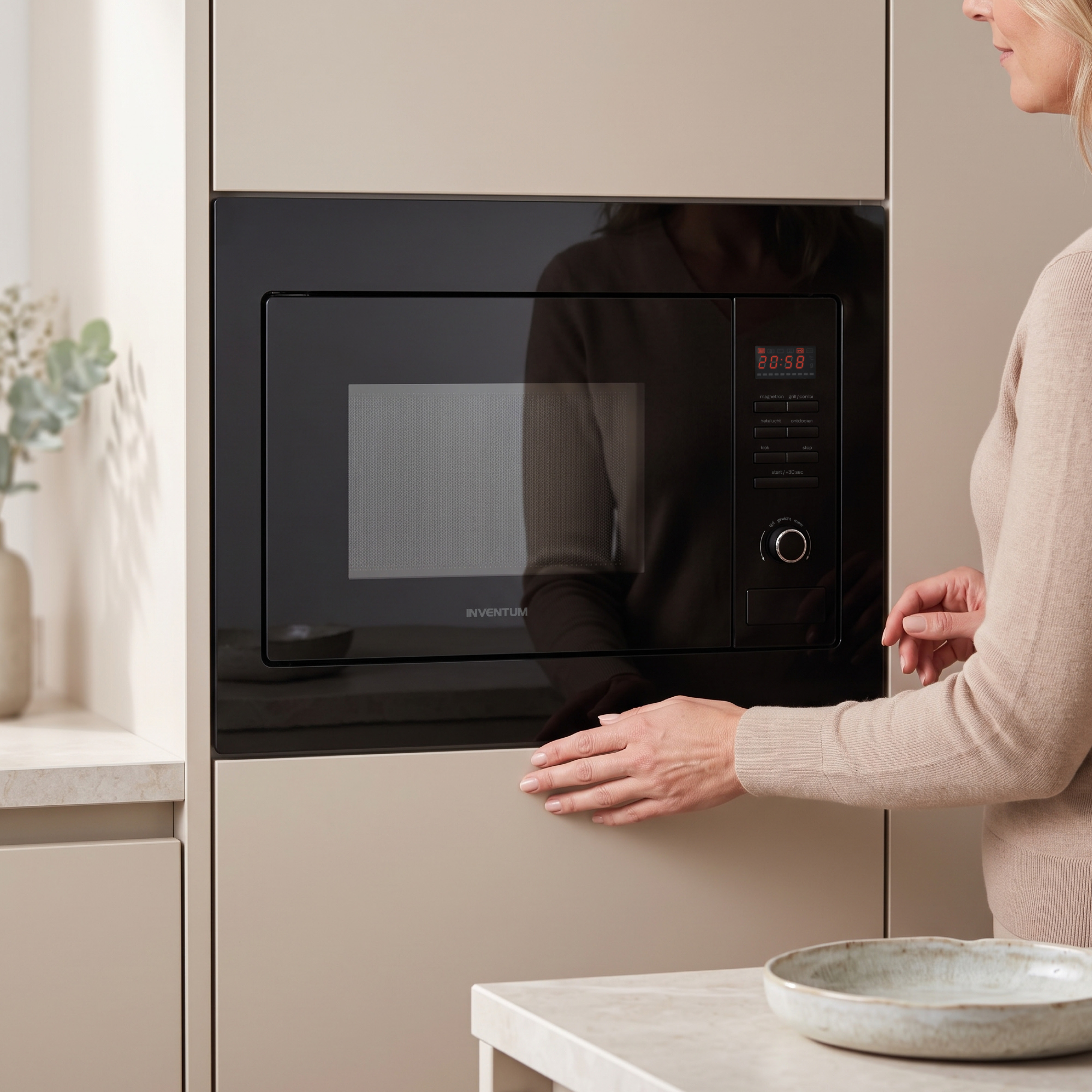 Une femme en pull beige ouvre un micro-ondes noir encastré Inventum dans une cuisine moderne.