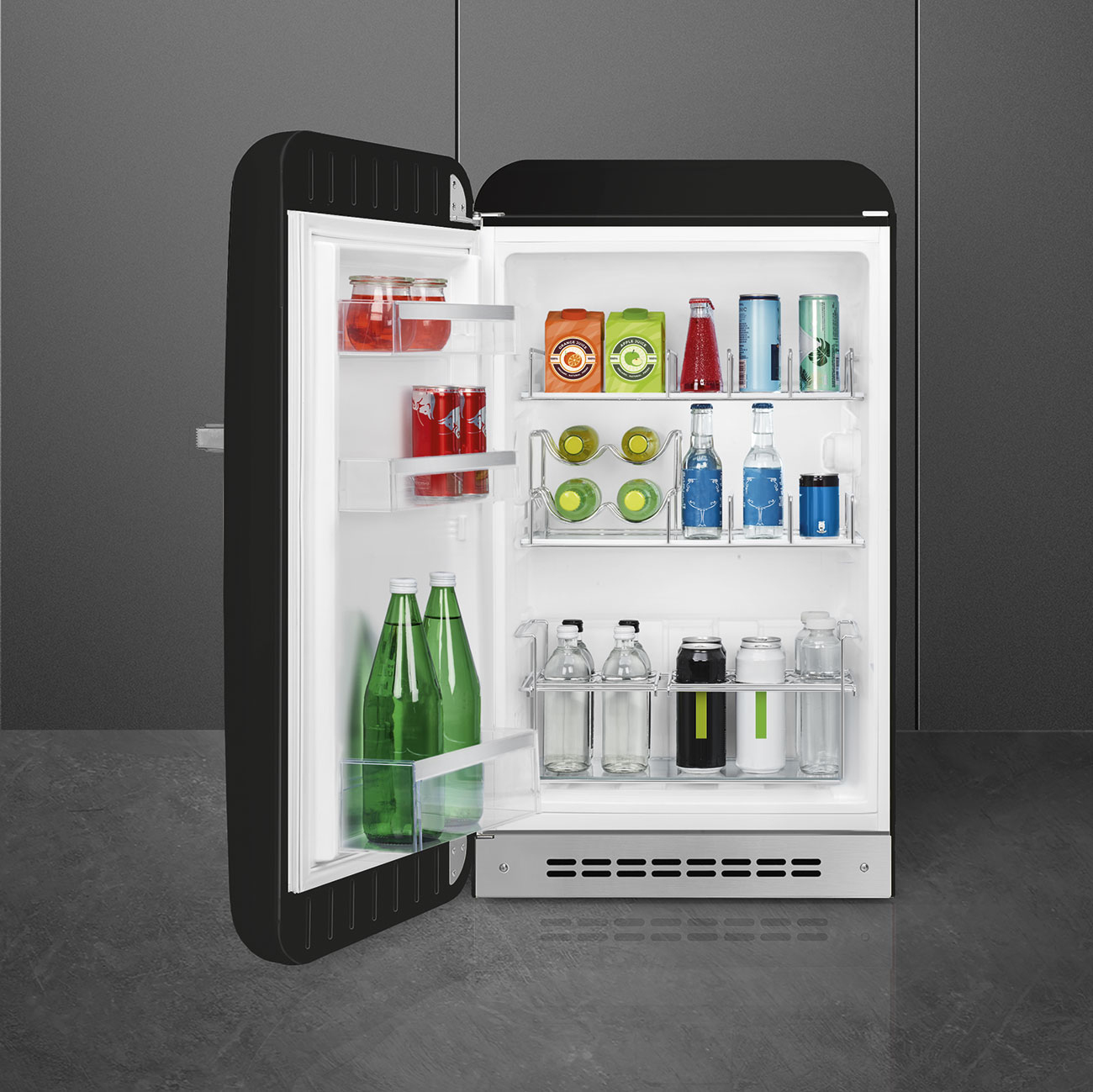 Un refrigerador retro negro abierto lleno de varias bebidas en sus estantes y puerta sobre un fondo gris.