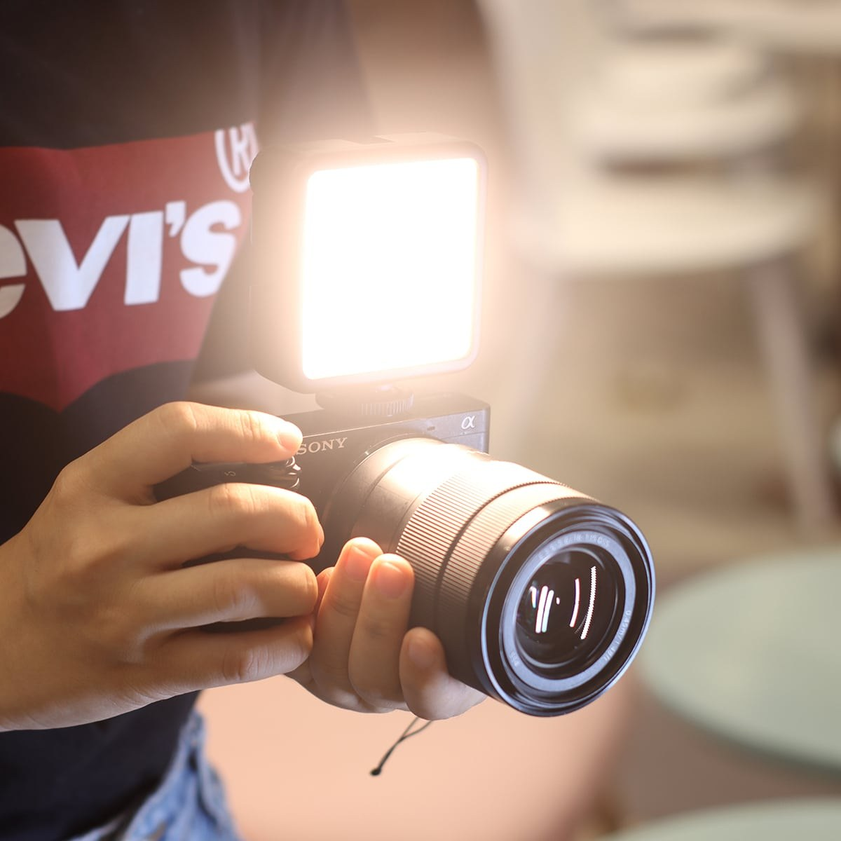 Una persona sostiene una cámara Sony negra con un panel de luz LED brillante encima, en interiores.
