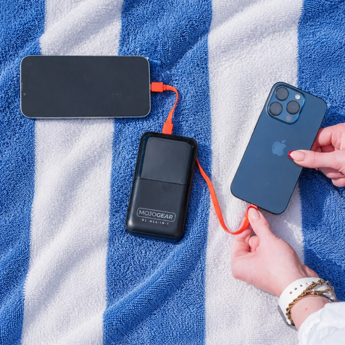 Eine Powerbank mit orangem Kabel lädt zwei Smartphones auf einer blau-weiß gestreiften Decke.