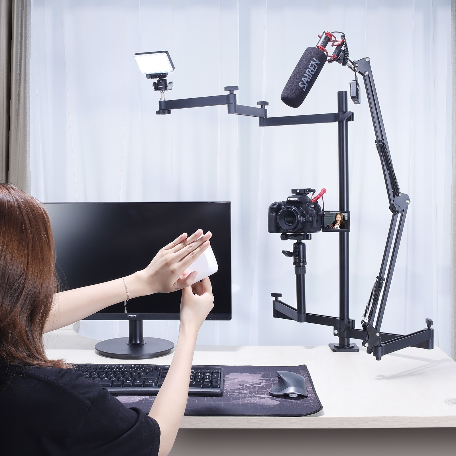 Une femme tient une boîte blanche sur un bureau avec un moniteur, un clavier et un support de caméra et de micro complexe.