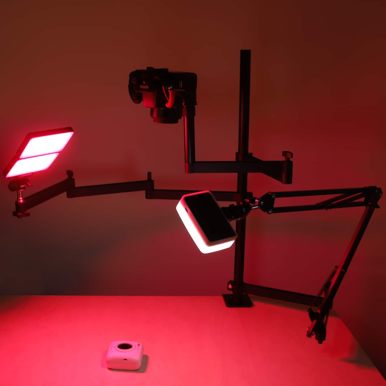 Support de caméra articulé avec deux panneaux LED sur une table, éclairé en rouge.