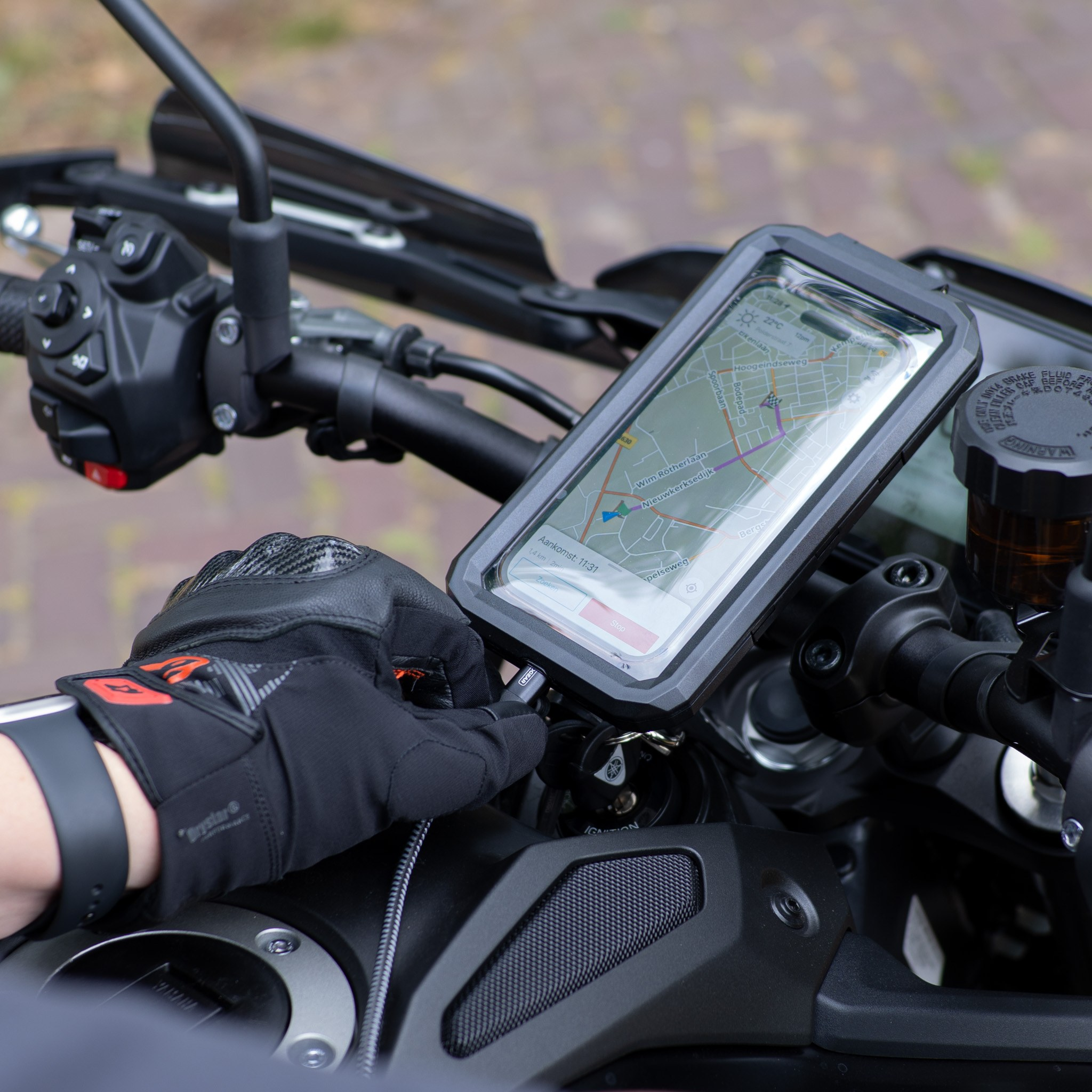 Guidon de moto avec un smartphone dans un support et une main gantée branchant un câble.