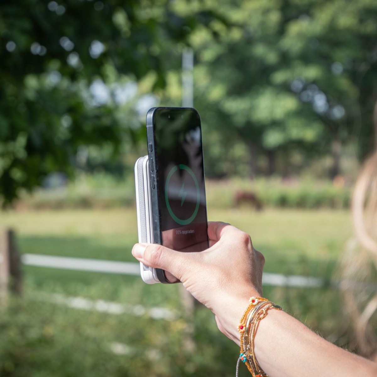 Eine Hand hält ein Smartphone mit einer Powerbank an einem grünen Hintergrund.