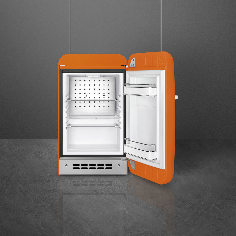 Un refrigerador retro naranja abierto sobre un piso oscuro contra una pared gris.