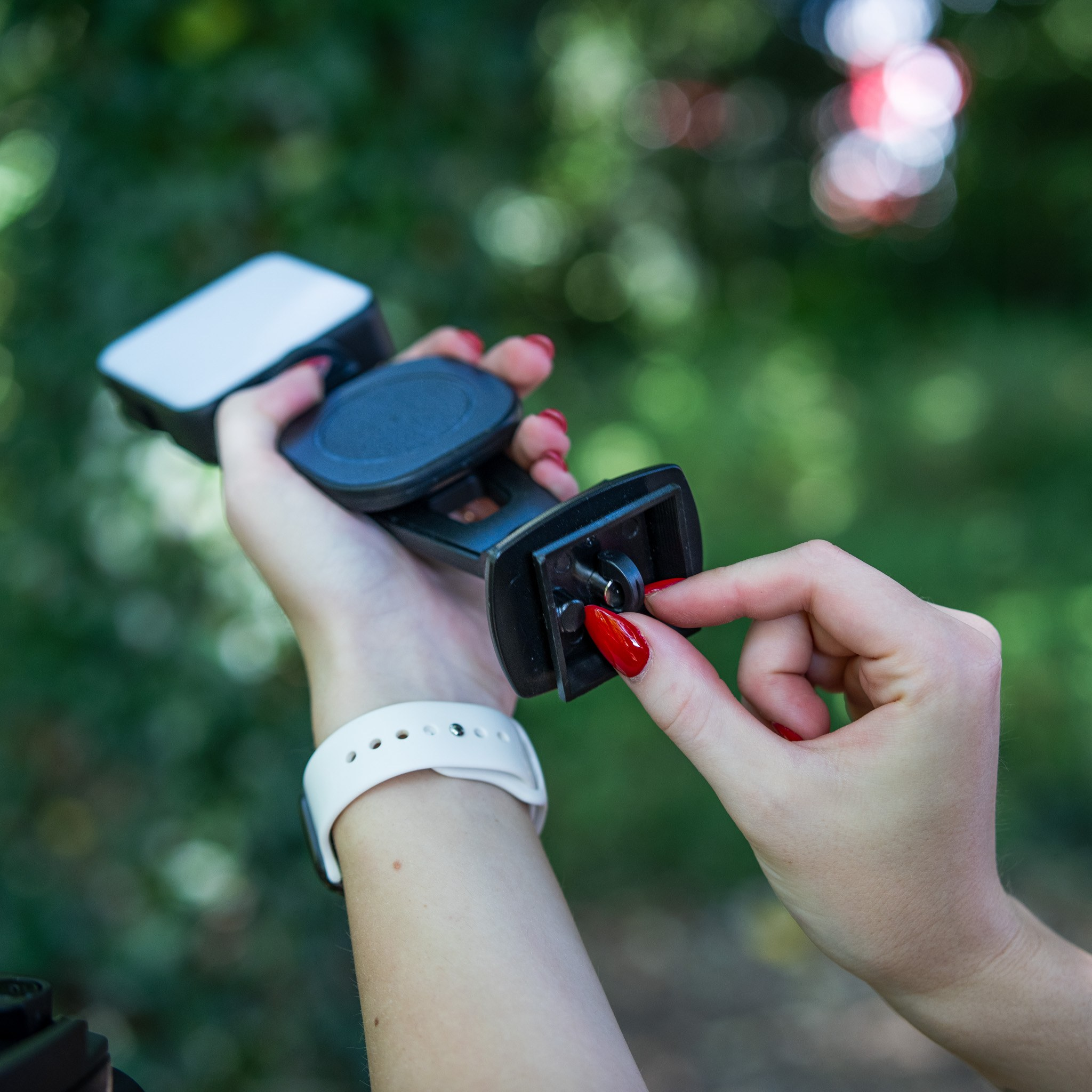 Person holding a black camera mount in one hand while adjusting a screw with the other hand outdoors.