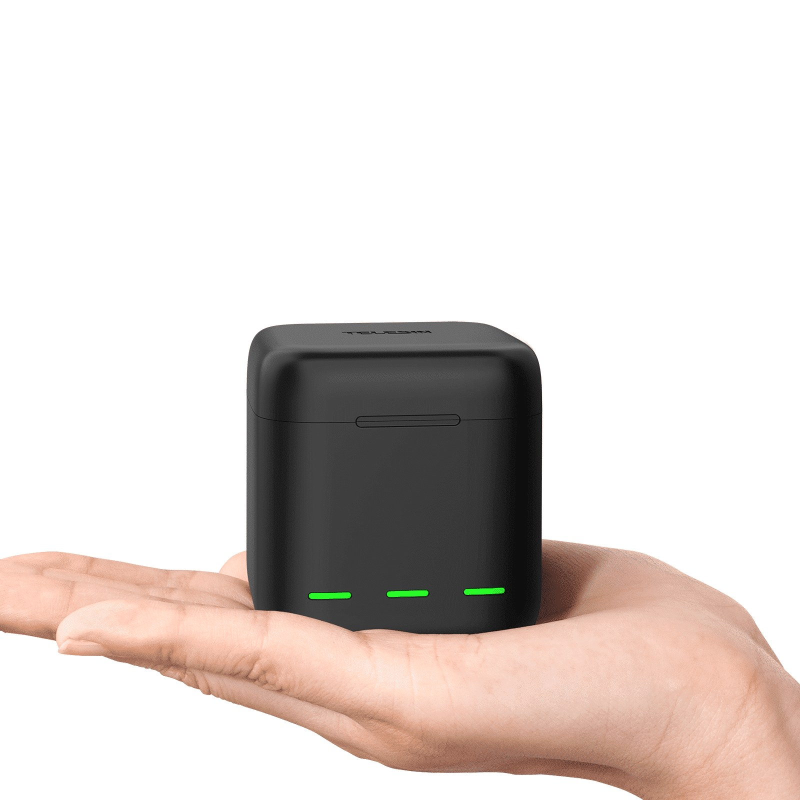 Una mano sostiene un pequeño estuche de carga Telesin negro con tres luces LED verdes sobre fondo blanco.