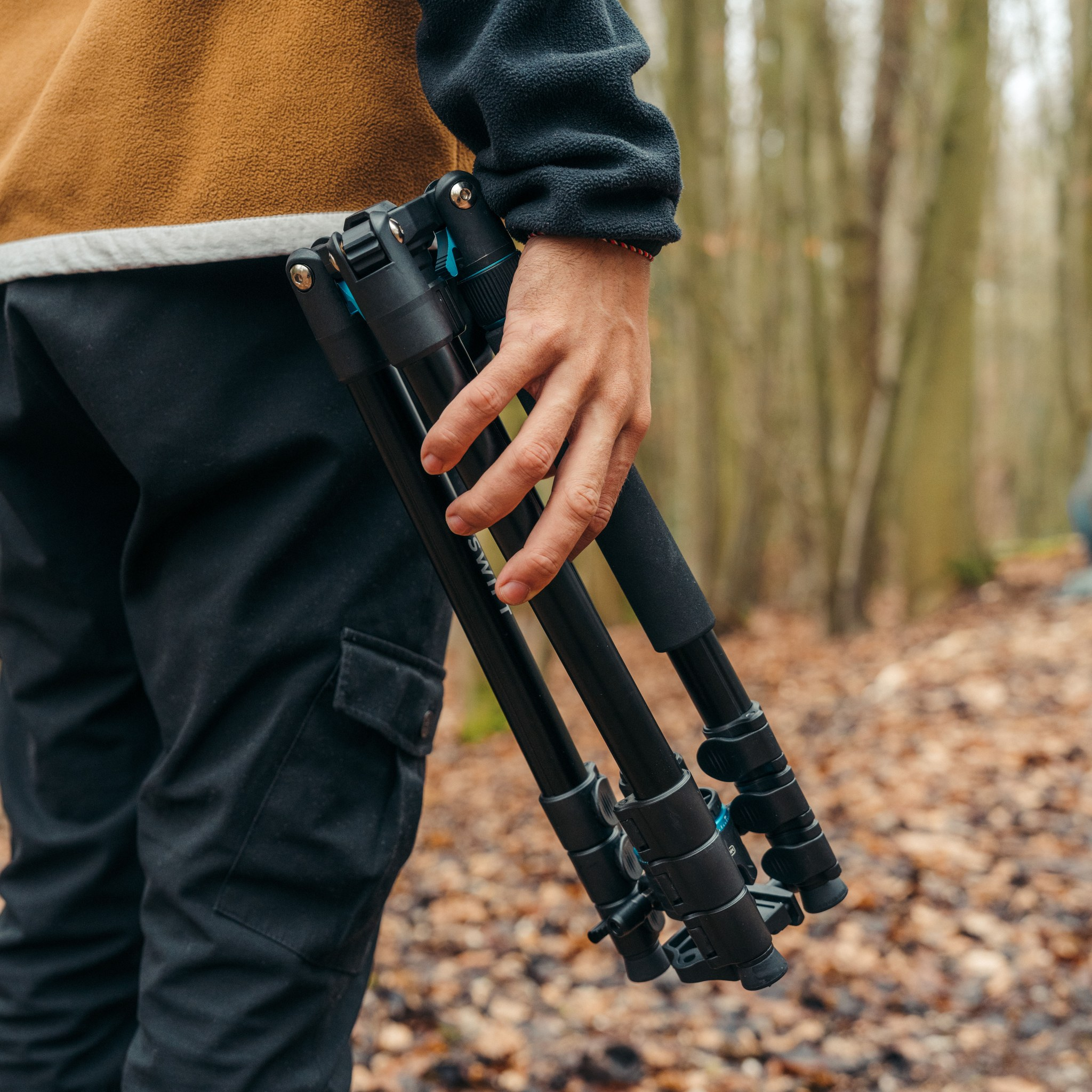 Une personne dans une forêt tient un trépied noir fermé à la main.