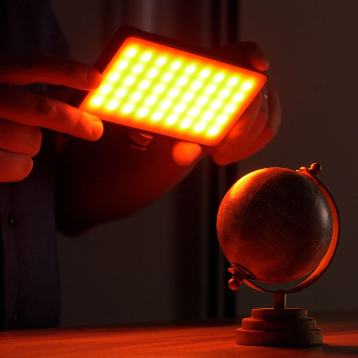 Iemand houdt een gloeiend LED-paneel vast dat een kleine wereldbol op een houten tafel verlicht.