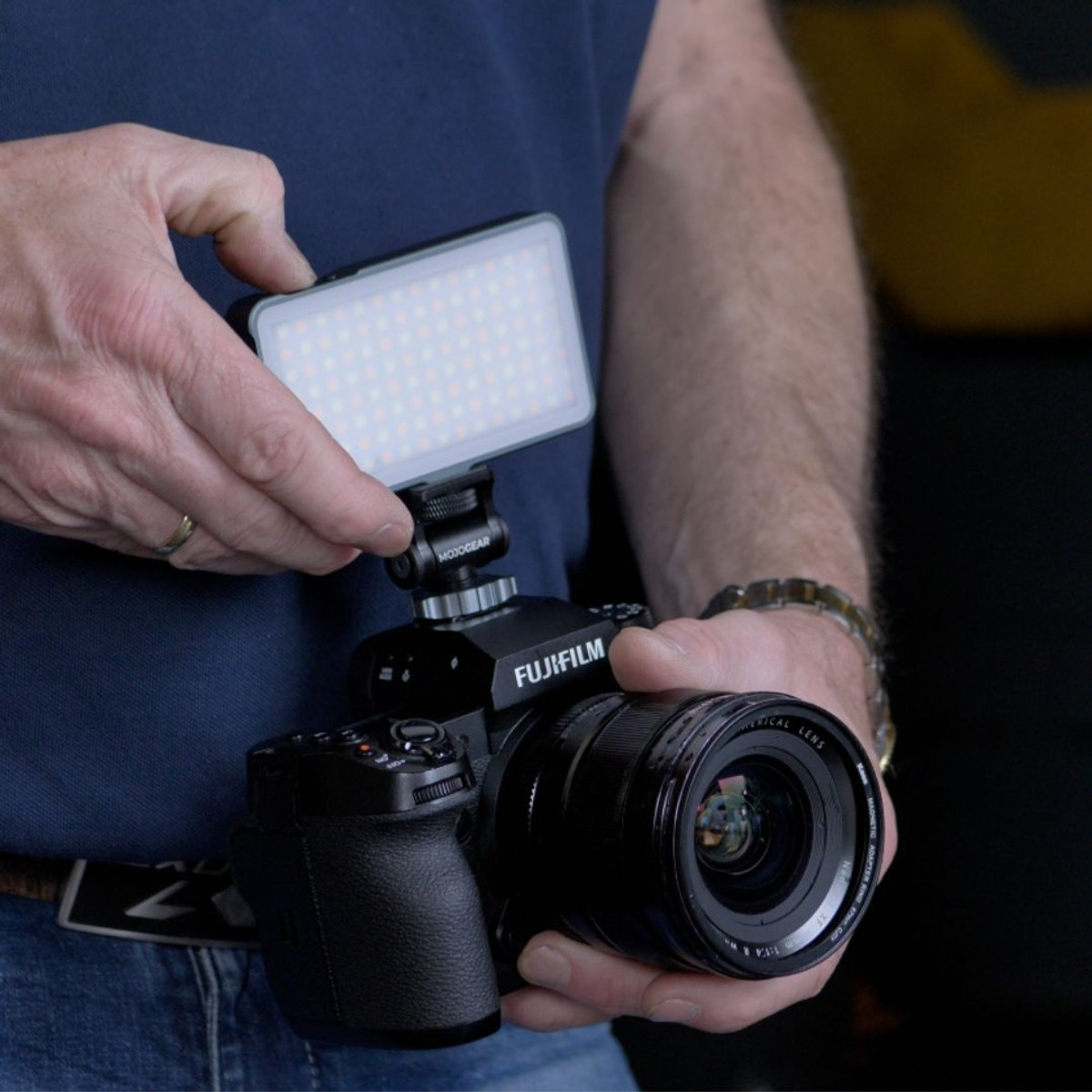 Persoon houdt een zwarte Fujifilm-camera vast met een klein LED-lampje op de flitsschoen.