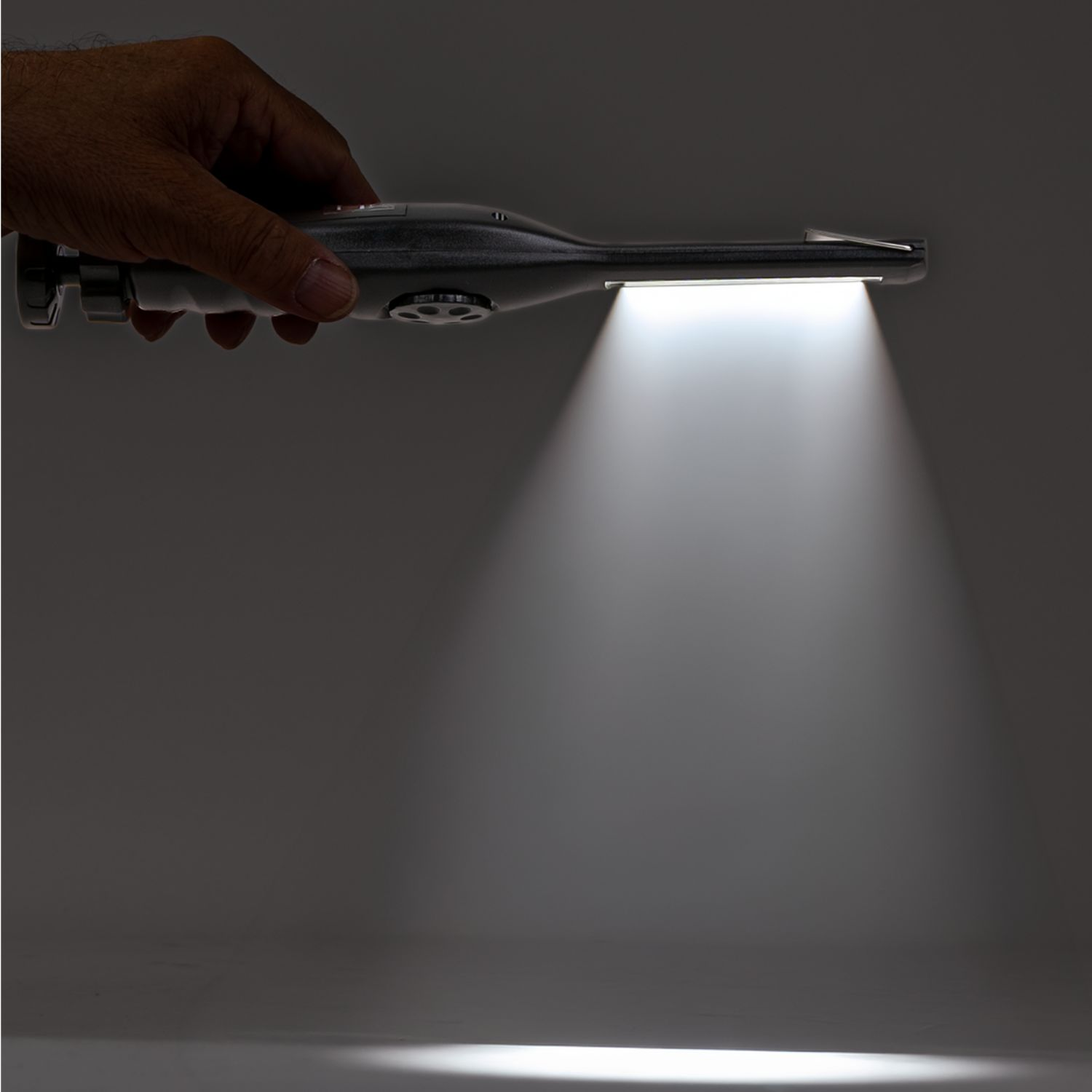 Eine Hand hält eine dunkle Lampe, die helles Licht auf eine Oberfläche wirft.