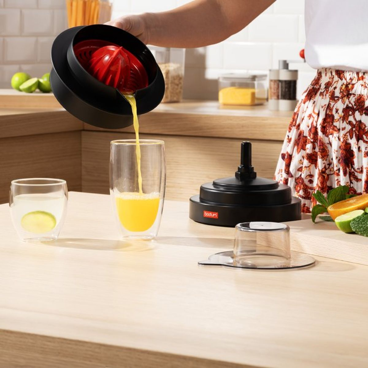 Eine Person gießt Orangensaft aus einer schwarzen und roten Presse in ein Glas.