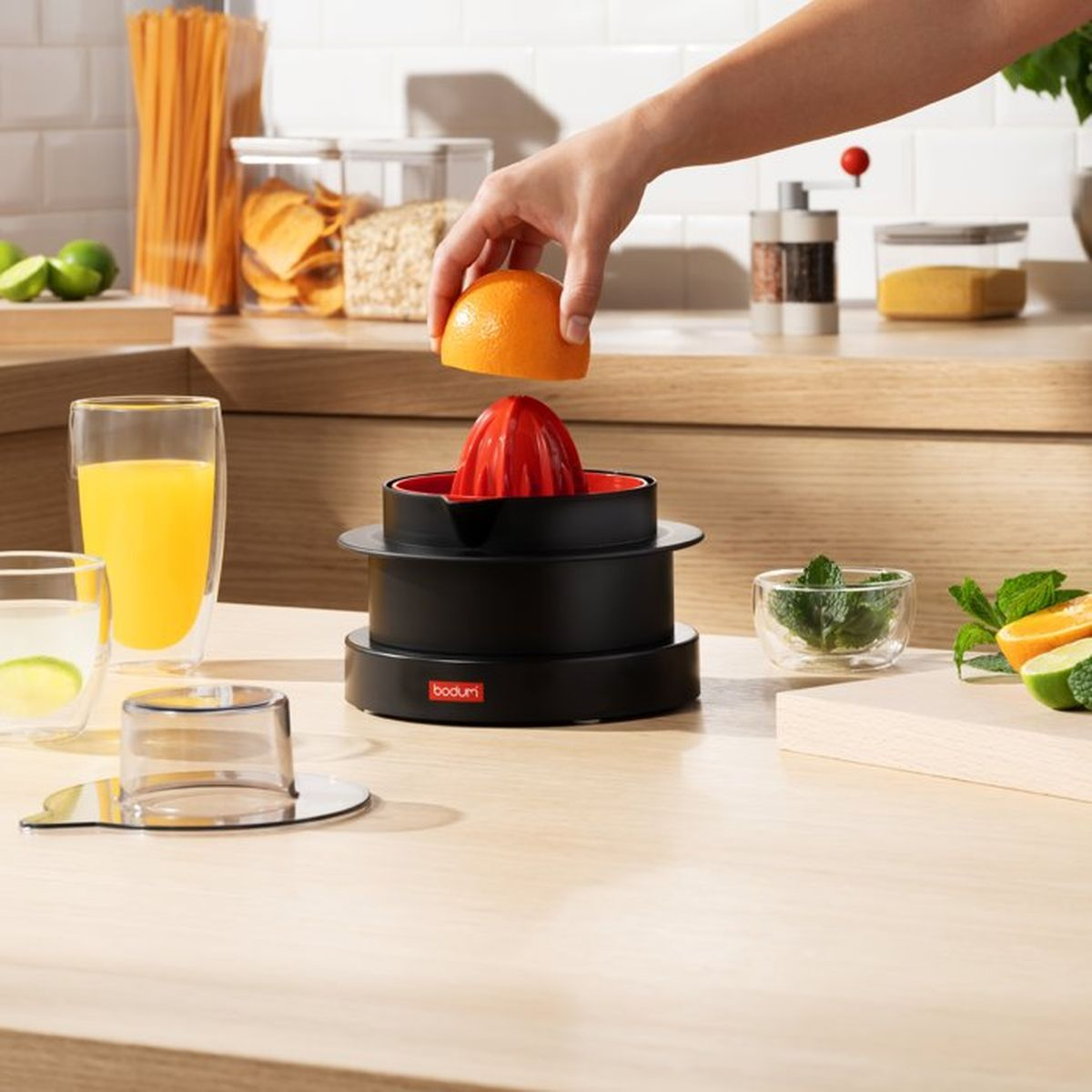 Eine Hand presst eine halbe Orange auf eine schwarze Zitronenpresse mit rotem Einsatz.