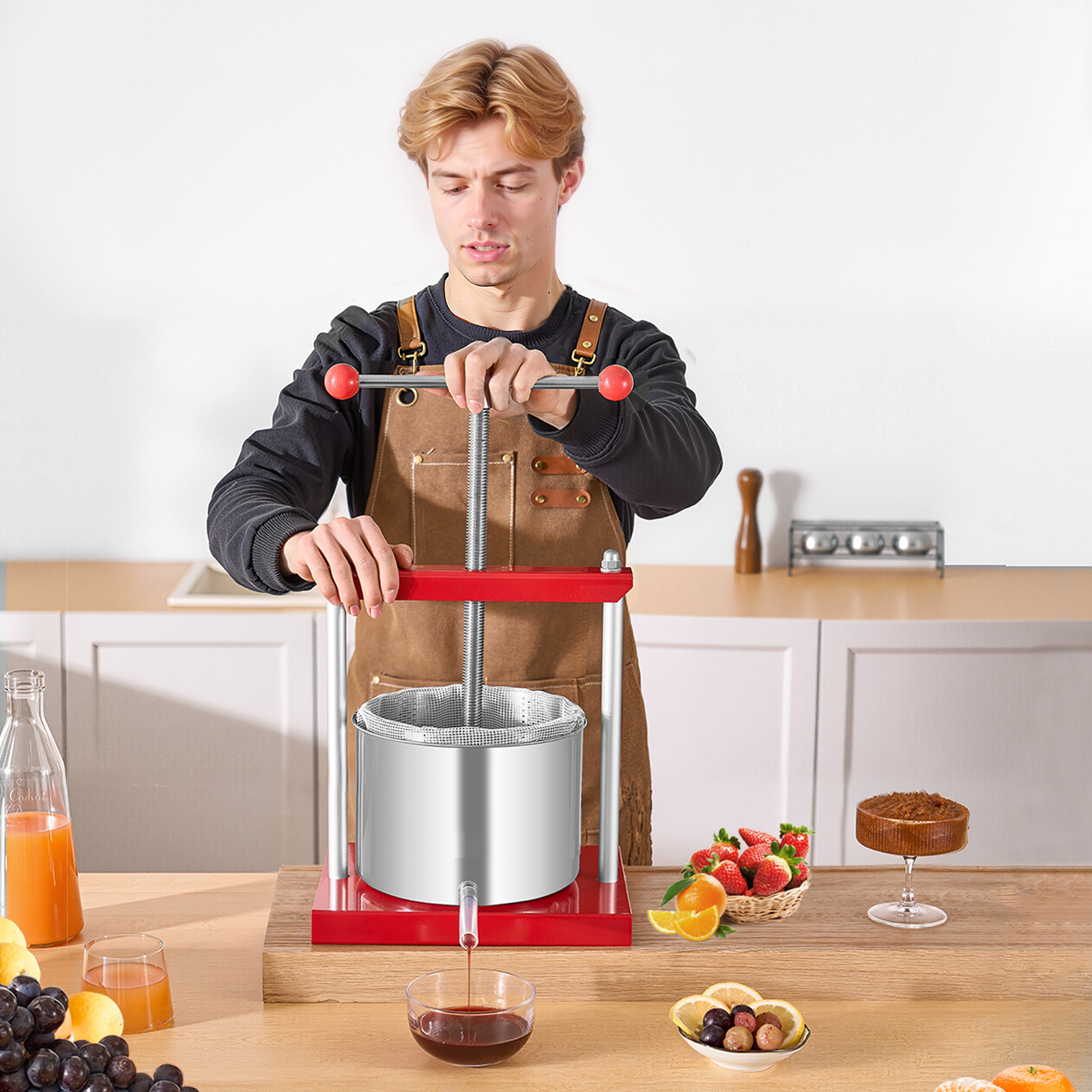 Un joven con delantal de cuero marrón usa una prensa manual de acero inoxidable para extraer jugo de frutas rojas.