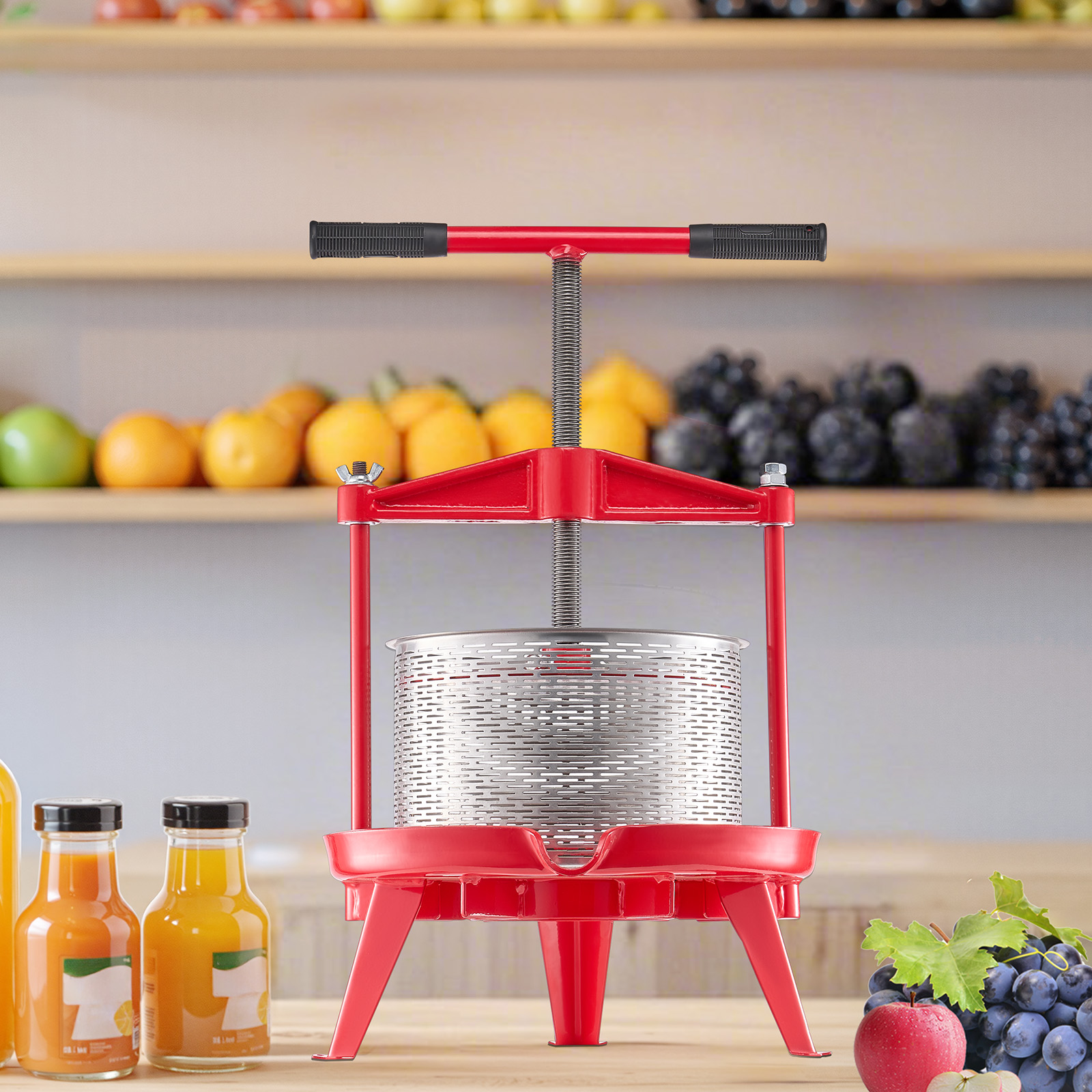 Prensa de fruta roja de metal con colador, botellas de jugo y fruta fresca en estantes al fondo.